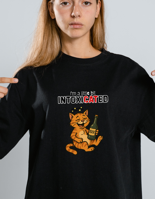 Young person wearing a black t-shirt with a cat graphic and text 'I'm a little bit INTOXICATED' on a plain background